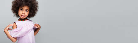 toddler african american girl in violet blouse and colorful beads posing isolated on grey, bannerの写真素材