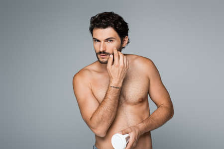 tattooed and shirtless man holding container and applying cosmetic cream isolated on greyの写真素材