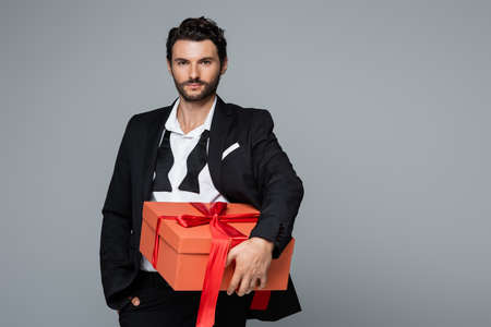 young bearded man in suit holding red present isolated on greyの写真素材