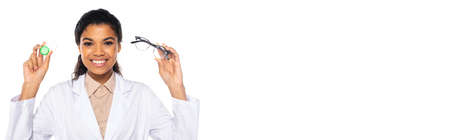 Happy african american doctor holding optical lenses and eyeglasses isolated on white with copy space, bannerの写真素材