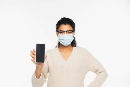 African american woman in eyeglasses and medical mask holding cellphone with blank screen isolated on whiteの写真素材
