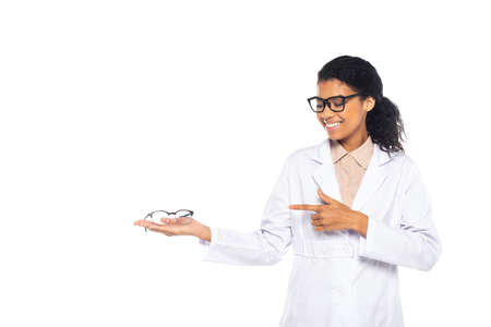 Smiling african american doctor pointing at eyeglasses on hand isolated on whiteの写真素材