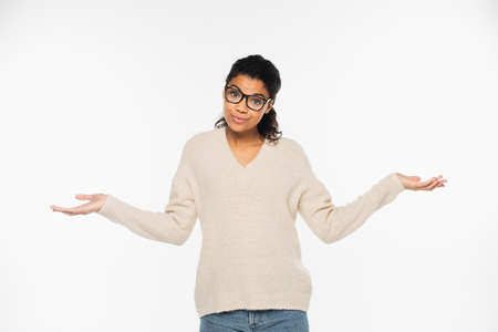 Confused african american woman in sweater and eyeglasses doing shrug gesture isolated on whiteの写真素材
