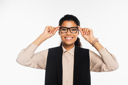 Cheerful african american manager holding eyeglasses and looking at camera isolated on whiteの写真素材