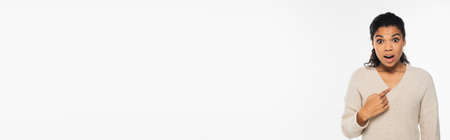Amazed african american woman in sweater pointing with finger isolated on white, bannerの写真素材