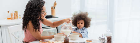 African american parent pouring milk in bowls near breakfast and toddler kid in kitchen, bannerの写真素材