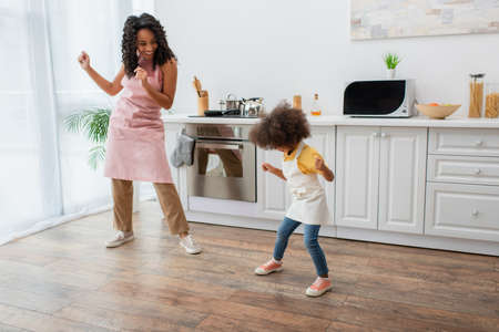 Happy african american woman and kid in aprons dancing in kitchenの写真素材