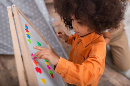 High angle view of african american child playing with signs on magnetic board near mom at home