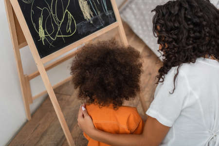 Overhead view of african american woman hugging child near chalkboard at homeの写真素材