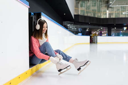 positive young woman tying shoe laces on ice skatesの写真素材