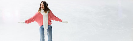 smiling young woman in ear muffs and scarf on ice rink, bannerの写真素材