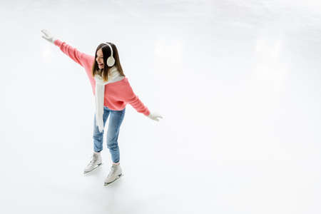 high angle view of happy young woman in ear muffs and scarf skating on ice rinkの写真素材