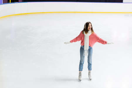 full length of amazed young woman skating with outstretched hands on ice rinkの写真素材