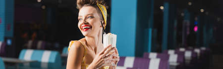 happy pin up woman holding milkshake in glass in cafe, bannerの写真素材