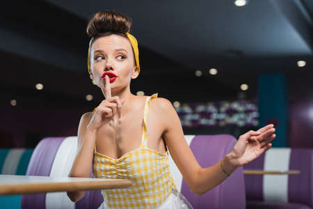 young pin up woman showing hush sign in vintage cafe