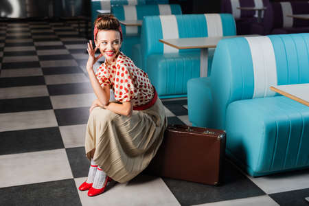 happy pin up woman sitting on vintage suitcase in cafeの写真素材
