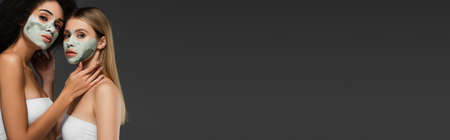 young interracial women with clay masks on faces looking at camera isolated on grey, bannerの写真素材