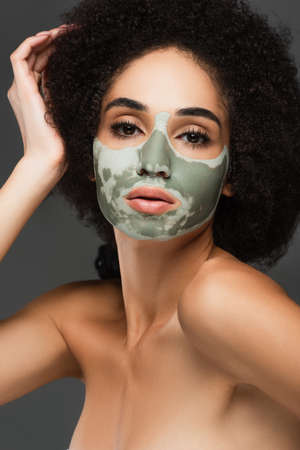 sensual african american woman with naked shoulders and clay mask on face looking at camera isolated on greyの写真素材