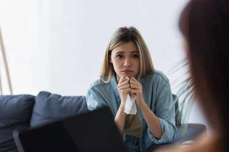 frustrated woman with paper napkin near psychologist with laptop on blurred foregroundの写真素材