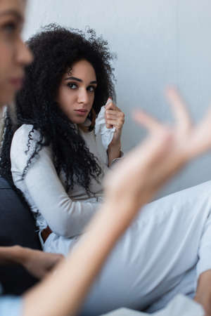 offended african american woman looking at blurred girlfriend talking during psychological consultationの写真素材