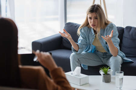 unhappy woman gesturing while talking to blurred psychologist in consulting room
