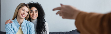 blurred psychologist pointing at smiling interracial lesbian couple during consultation, bannerの写真素材