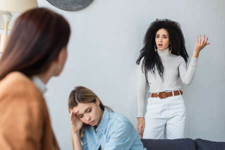 african american lesbian woman quarreling near depressed girlfriend and blurred psychologistの写真素材