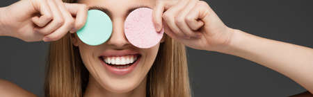 smiling woman obscuring eyes with cosmetic sponges isolated on grey, bannerの写真素材
