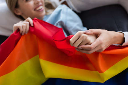 cropped view of lesbian woman holding hand of blurred girlfriend with lgbt flagの写真素材