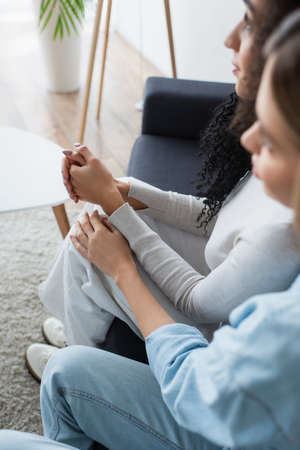 blurred interracial lesbian couple sitting together on sofaの写真素材