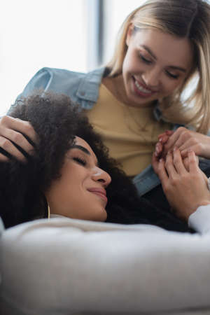 blurred lesbian woman touching hair and holding hands of happy african american girlfriendの写真素材
