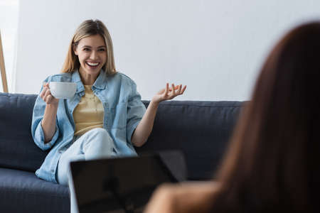 happy woman with cup of tea talking to psychologist on blurred foregroundの写真素材