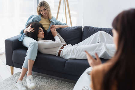 blurred psychologist near happy interracial lesbian couple on couch in consulting roomの写真素材