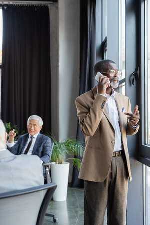 senior african american businessman talking on cellphone near colleagues working on blurred backgroundの写真素材