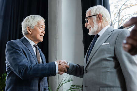 senior interracial business partners smiling while shaking hands in office