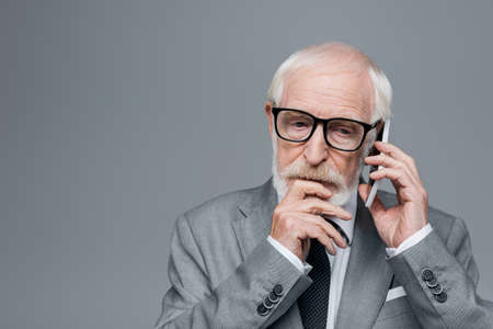 thoughtful elderly businessman talking on mobile phone isolated on grey