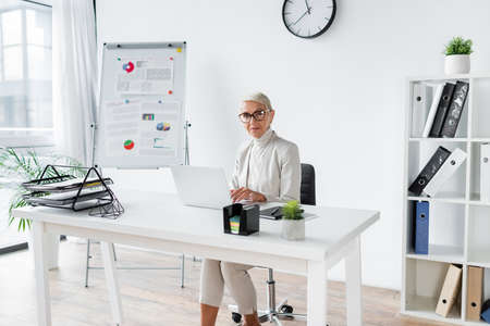 businesswoman with grey hair using laptop in modern officeの写真素材