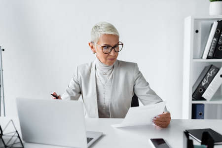 senior businesswoman in glasses looking at document in office