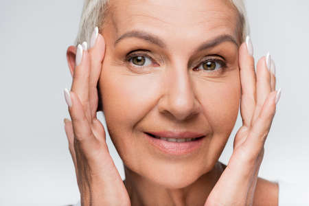 positive senior woman looking at camera isolated on grey