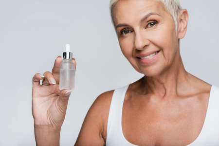 happy elderly woman holding bottle with serum isolated on greyの写真素材