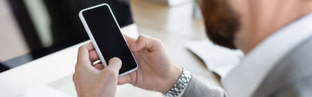Cropped view of businessman using cellphone with blank screen in office, bannerの写真素材