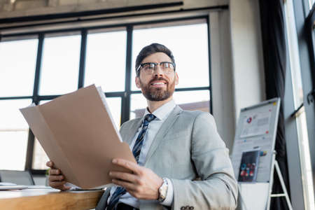 Smiling businessman in suit holding paper folder in office