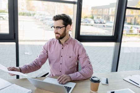 Businessman working with documents near devices and coffee in officeの写真素材
