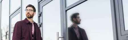 Businessman in trench coat walking near building on urban street, banner