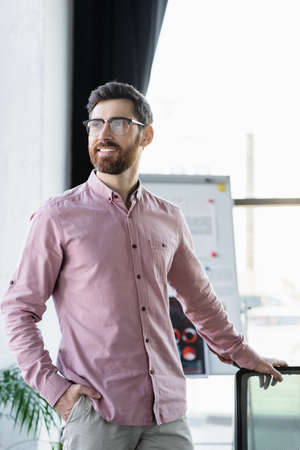 Positive businessman in eyeglasses standing in office