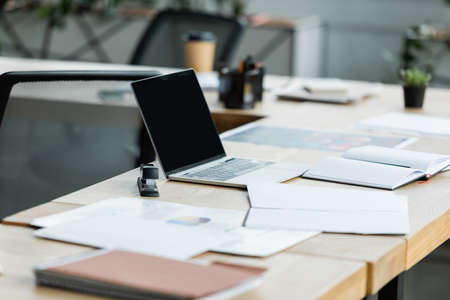 laptop with blank screen near empty notebook and documents on office deskの写真素材