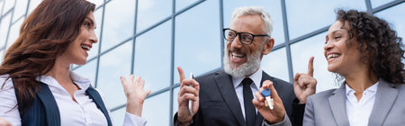 happy african american businesswoman holding key near excited colleague and realtor pointing at...