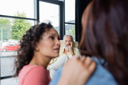middle aged psychologist looking at lesbian couple on blurred foreground in consulting roomの写真素材