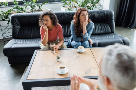 interracial lesbian couple with relationship difficulties sitting on couch during appointment with psychologistの写真素材