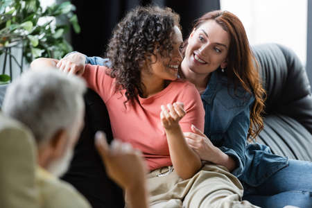 blurred psychologist near happy interracial lesbian couple sitting on sofa during consultation